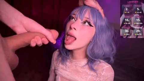 Media: A video of a pale-skinned woman with blue hair, wearing a white lace top, licking a man's erect penis. Background is dimly lit with purple hues.