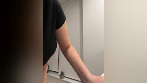 Media: A video showing a person in a black shirt reaching toward a mirror in a minimalist, white-walled bathroom. A small potted plant sits on the white counter.