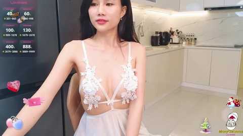 Media: Video of an Asian woman with long black hair, wearing a sheer white lace lingerie bodysuit with floral embroidery, standing in a modern kitchen.