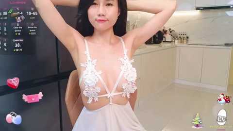 Media: Video of an East Asian woman with long black hair, wearing a revealing white lace lingerie with floral patterns, posing in a modern kitchen.