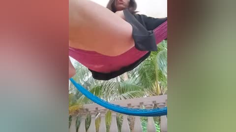 Media: A video shows a woman's legs in pink underwear and a black top, hanging from a hammock in a lush tropical garden with palm trees.