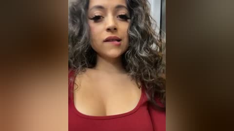 Media: Video of a light-skinned woman with curly brown hair, wearing a low-cut red top, speaking with a neutral expression.