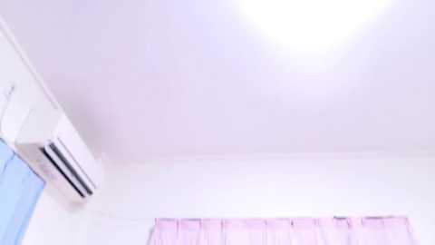 Media: Video of a minimalist room with a white ceiling, a large air conditioner unit, and light blue curtains. The room has a clean, uncluttered look.