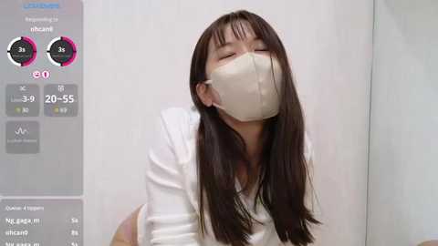 Media: Video of an Asian woman with long dark hair and light skin, wearing a white mask, white shirt, and a white background.