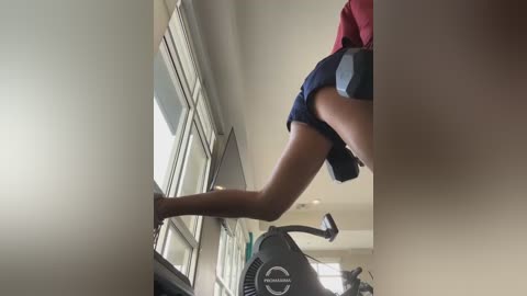 Media: A video of a person with a slim physique, wearing dark shorts, performing a high kick on a treadmill in a bright, minimalist room with large windows.