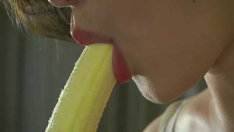 Media: Video of a close-up of a woman with light skin and brown hair, biting into a juicy yellow melon, showing her red lipstick and bare shoulders.