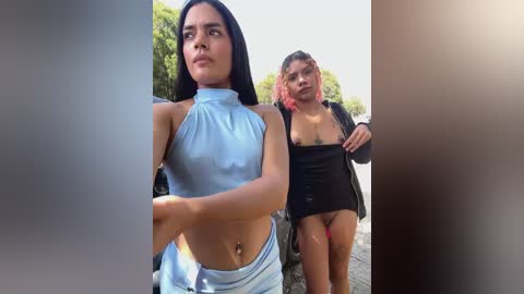 Media: Video of two women walking outside. The woman on the left wears a light blue halter top and white shorts, with medium skin tone and long black hair. The woman on the right has a medium skin tone, short hair, and wears a black crop top and red bikini bottoms.