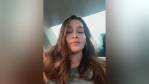 Media: A video of a young Caucasian woman with long, wavy brown hair, light skin, and a relaxed expression, captured from a slightly elevated angle, showing her partially obscured face.