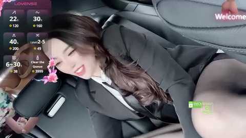 Media: A video of a woman with long brown hair, wearing a black suit and white shirt, lying seductively in a car, with a digital screen showing \"Live\" and \"WeChat\" in the background.