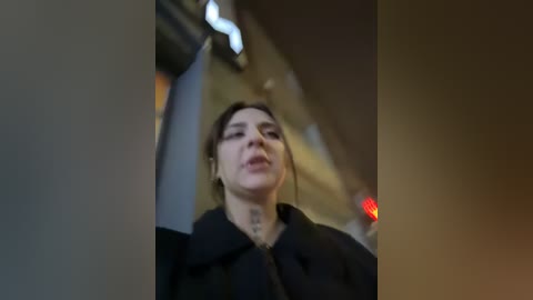 Media: Video of a woman with light skin and brown hair, wearing a black coat, looking upwards, in an urban setting with blurred background lights.