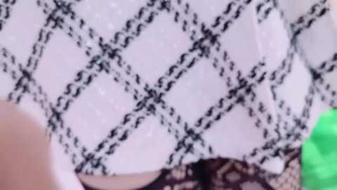 Media: Video of a close-up view of a woman's upper body, wearing a white, black diamond-patterned top with black lace trim. The background is blurred, showing green and white objects.