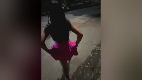 Media: A video of a woman with dark skin, wearing a pink skirt, standing confidently on a sidewalk. Her black hair is styled in braids, and she has a slim, toned physique. The background features a concrete pathway and scattered leaves.