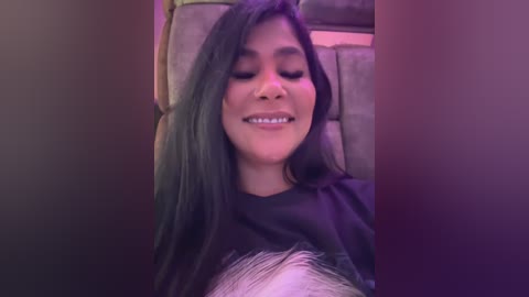 Media: Video of a young woman with long, dark hair, wearing a black top, smiling and lying back in a car seat, bathed in purple light.