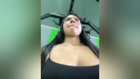 Media: A video of a curvy, dark-haired woman in a black sports bra, lifting weights in a gym with green and white walls.