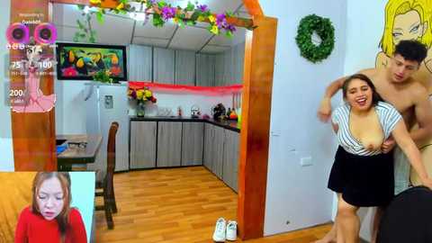 Media: Video of a playful, semi-nude couple in a colorful, modern kitchen; wooden floor, vibrant wall art, and a green wreath.