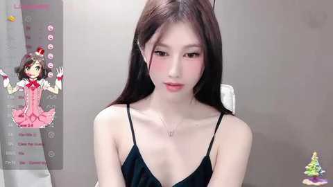 Media: Video of a young Asian woman with long black hair, wearing a black spaghetti-strap dress, sitting indoors, overlaid with a digital character in a pink dress.