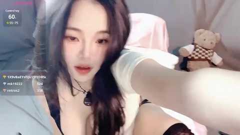 Media: A video of an Asian woman with long black hair, wearing a white top, black lace panties, and a dog toy. She's on a bed with a soft pink blanket, taking a selfie.