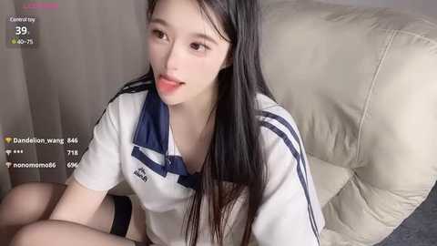 Media: A video of a young East Asian woman with long black hair and fair skin, wearing a white Adidas shirt, sitting on a beige couch. Text overlay shows live streaming information.