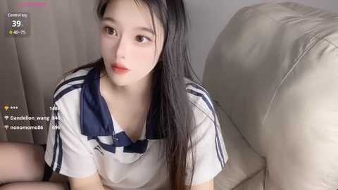 Media: A video of an East Asian woman with long black hair, fair skin, and a light blue and white sailor-style top, lying on a beige couch. The background features soft, muted tones.