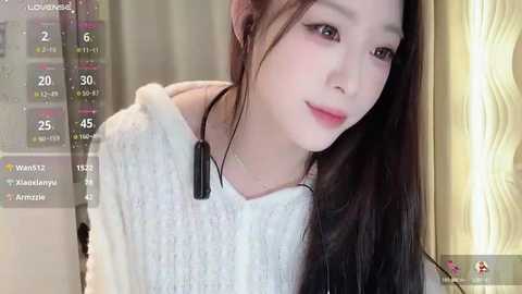 Media: Video of a young Asian woman with long black hair, wearing a white sweater, smiling softly, with a digital screen overlay displaying social media metrics.