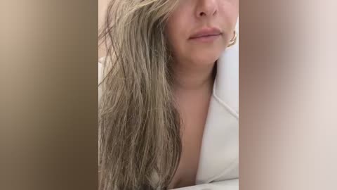 Media: A video of a woman with long, wet, light brown hair, partially covering her face. She has a light skin tone and is wearing a white top. The background is blurred, with neutral tones.