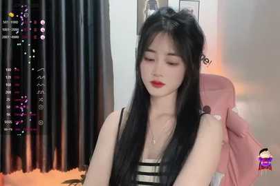 Media: Video of a young Asian woman with long black hair, wearing a sleeveless striped top, sitting on a pink chair, in a dimly lit room with black curtains and a colorful background.