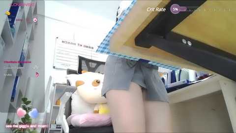 Media: A video of a person's legs wearing grey shorts and a plush white cat sitting on a chair in a brightly lit office.