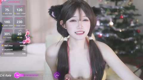 Media: Video of a young East Asian woman with long black hair styled in twin braids, wearing a revealing black and white bikini with cat ears. She smiles playfully in front of a festive Christmas tree.