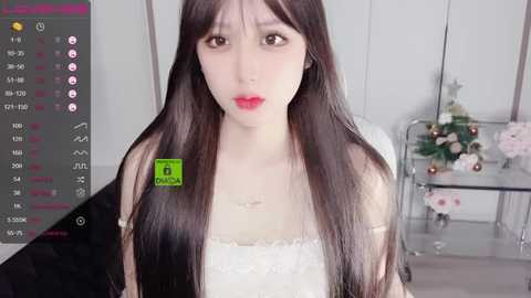 Media: Video of a young, fair-skinned Asian woman with long, straight, dark hair, wearing a white lace dress, standing indoors in front of a glass table with floral arrangements.