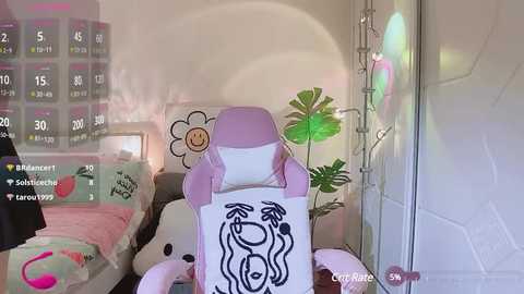 Media: A video of a cozy bedroom featuring a pink gaming chair, a white bed with plush toys, and a green plant. The room is lit by soft, pastel-colored lights.