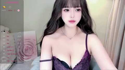 Media: A video of a young Asian woman with long black hair and pale skin, wearing a purple lace bra, in a bedroom with a pink rose-printed wall.