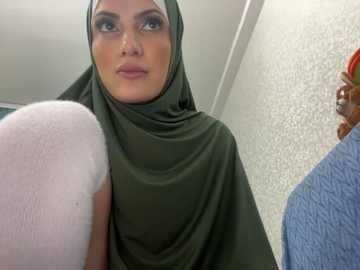 Media: Video of a woman with olive skin and dark eyes wearing a green hijab, holding a white foam soap in her right hand, in a white-tiled bathroom with a blue towel.