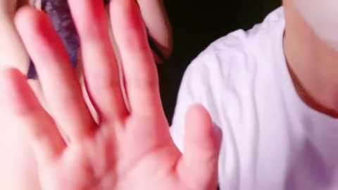 Media: Video of a person's hand with red nail polish making a claw gesture, resting on a white shirt sleeve against a dark background.