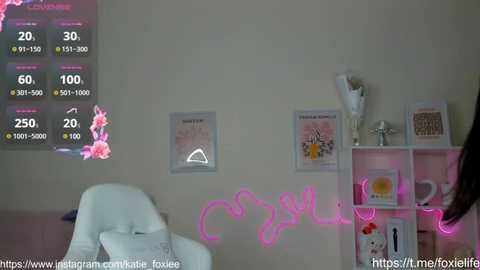 Media: A video of a cozy, pink-lit room with a white armchair, a digital thermometer, and a white bookshelf adorned with framed artwork.