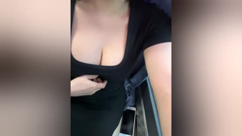 Media: Video of a light-skinned woman in a low-cut black top, revealing ample cleavage, seated in a car. She is adjusting her top. Background shows car interior with a smartphone on the dashboard.