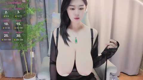 Media: Video of an East Asian woman with large, augmented breasts, wearing black lingerie and a sheer top, in a living room with a bamboo plant and curtains.