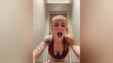 Media: A video of a young woman with light skin, red hair tied in pigtails, wearing a maroon sports bra and white shorts, leaping forward in a hallway, displaying a tattooed arm.