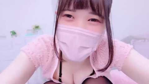 Media: Video of an Asian woman with fair skin, wearing a pink lace top, black bra, and a pink face mask, with long brown hair, in a bright, minimalistic room.