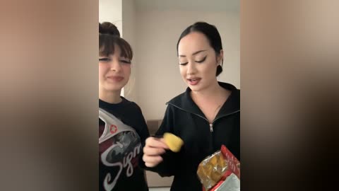 Media: Video of two young Asian women in a modern living room, one with a ponytail, the other with straight hair. They are eating popcorn and smiling.