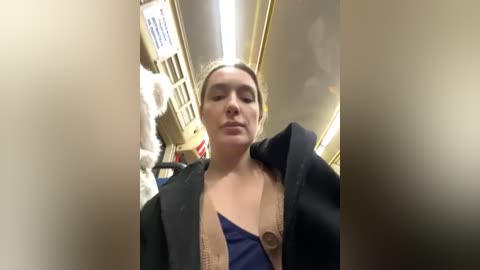 Media: A video of a woman with light skin and blonde hair, wearing a black jacket, standing in a subway car with beige walls, and a stuffed animal in the background.