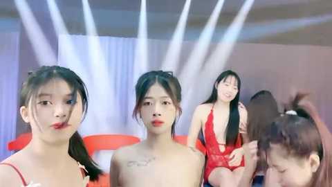 Media: Video of four young Asian women with long black hair, wearing red lingerie, standing in a brightly lit, modern indoor setting with white curtains and spotlights.