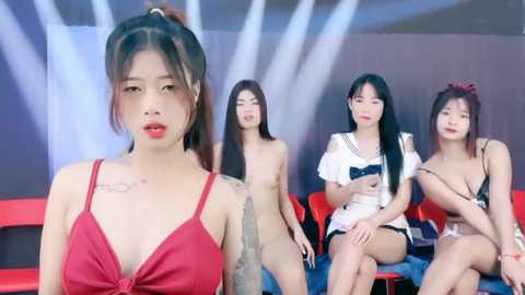 Media: Video of four East Asian women in lingerie on a red couch, one wearing a red bra, others in white and black lingerie, background with bright lights.