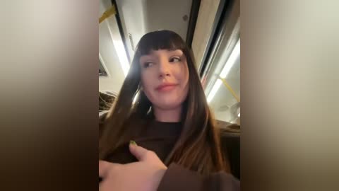 Media: A video of a young woman with straight, dark brown hair, blunt bangs, and a black top, sitting in a dimly lit bus.