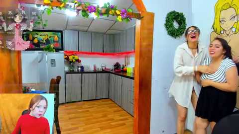 Media: Video of a cheerful woman in a striped top and another woman in a white shirt, laughing in a modern kitchen with gray cabinets, wooden floors, and colorful decorations.