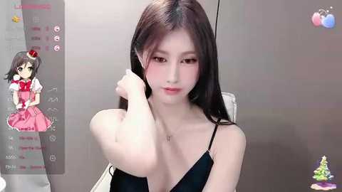 Video of a young Asian woman with long black hair, pale skin, and large breasts, wearing a black dress, sitting in front of a gray wall.