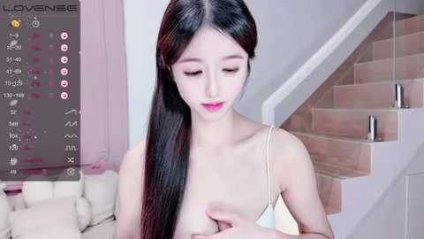 Media: Video of an East Asian woman with long black hair, wearing a white spaghetti strap top, covering her small breasts. Background features a staircase and a virtual \"LoveSense\" interface.