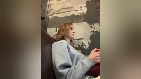 Media: A video of a Caucasian woman with wavy, shoulder-length red hair, wearing a light blue sweater, sitting on a train, looking out the window at an abstract cityscape.