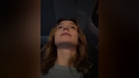 Media: Video of a young woman with long, wavy blonde hair lying in a car seat, looking up with a serene expression. The dimly lit interior suggests a nighttime drive.