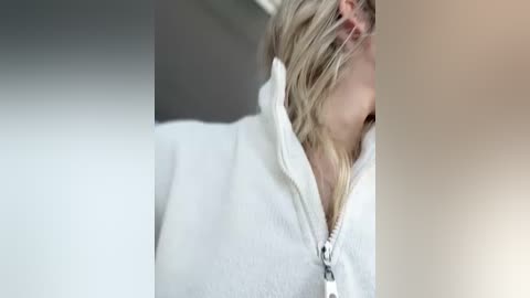 Media: A video of a partially visible blonde woman with a white hoodie, her face hidden by her hair, against a blurred background in soft, muted colors.