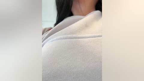 Media: Video of a close-up of a person's upper chest in a white shirt, with a blurred background. The person has long, dark hair visible at the top.